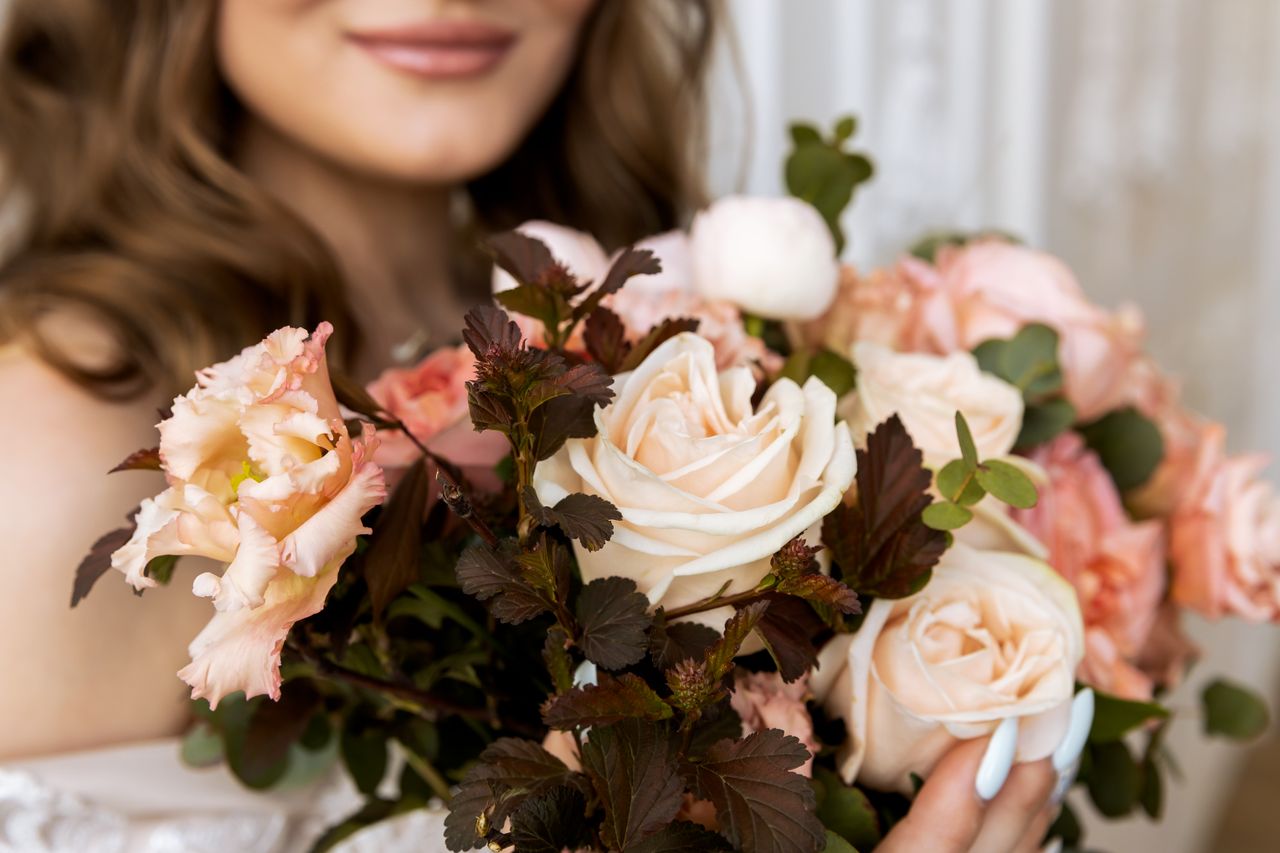 Close-up of a woman holding an elegant bouquet of blooming roses and flowers.
